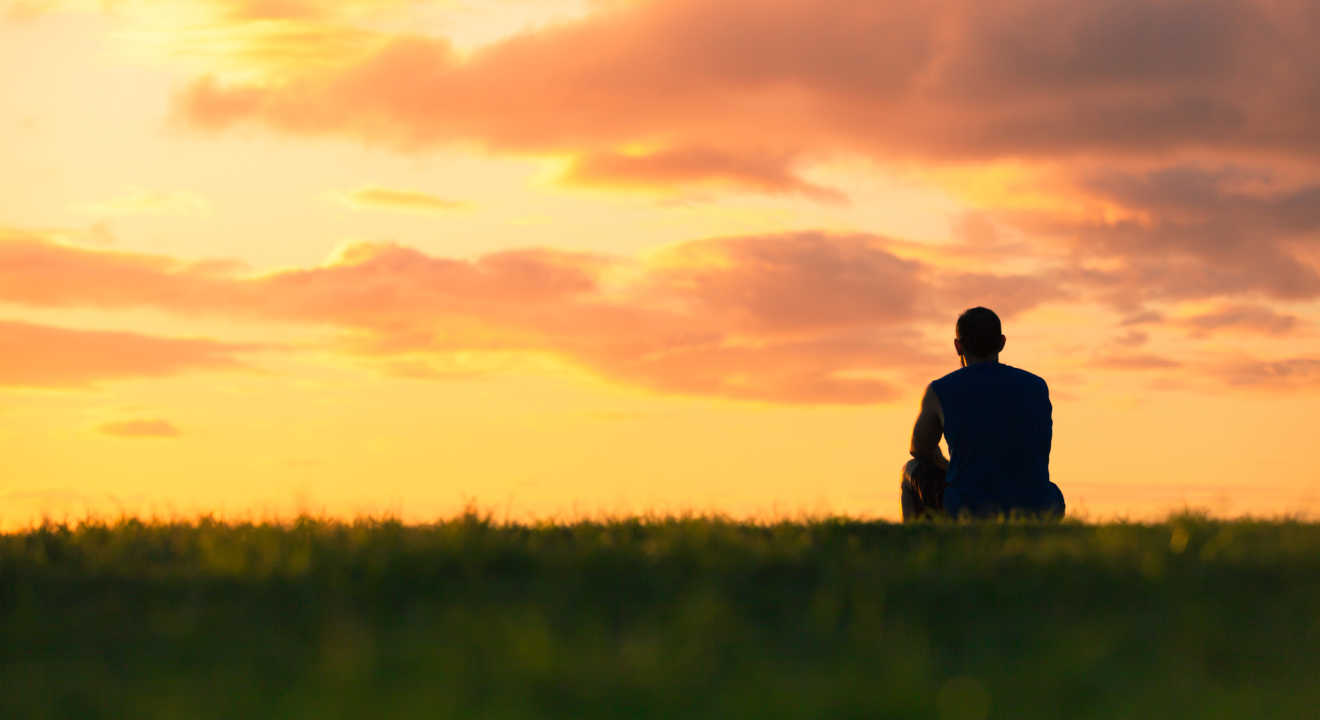 A man sitting alone looking out at a sunset