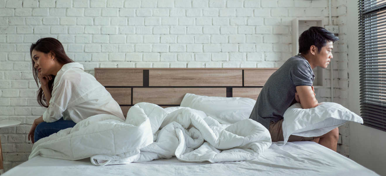 A couple sitting on a bed away from each other